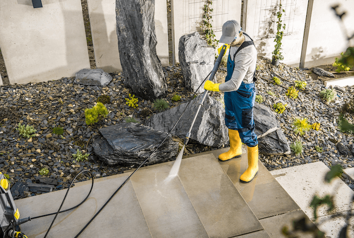 man pressure washing a cement walkway